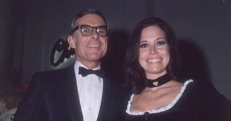 sekitar tahun 1975: Aktor Amerika Mary Tyler Moore, dalam gaun hitam dan choker, dan suami keduanya, eksekutif televisi Amerika Grant Tinker, berdiri berdampingan dan tersenyum. Tinker mengenakan tuksedo. (Foto oleh Hulton Archive/Getty Images)