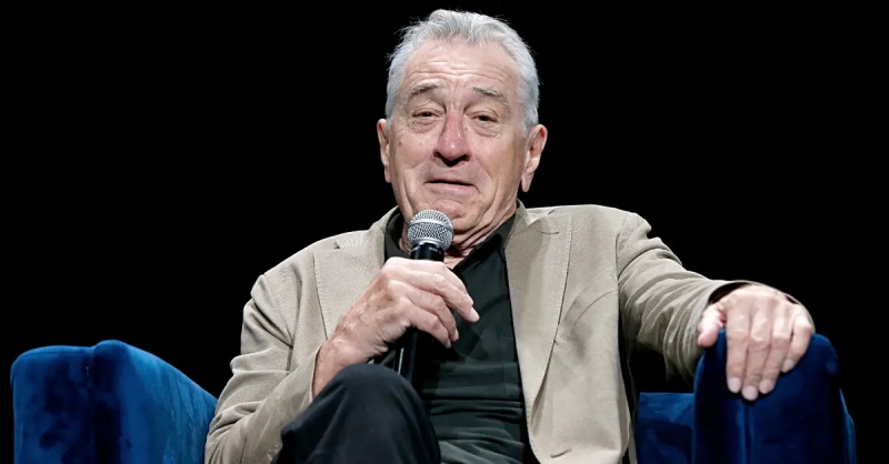   Robert DeNiro w brązowej kurtce przemawia na scenie