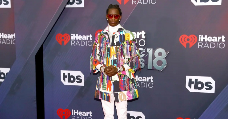 2018 iHeartRadio म्यूजिक अवार्ड्स में रंगीन जैकेट और धूप के चश्मे में पोज़ देता युवा ठग।