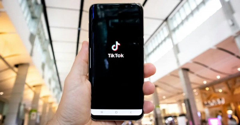 Людина тримає телефон у повітрі із завантаженим додатком TikTok на екрані.