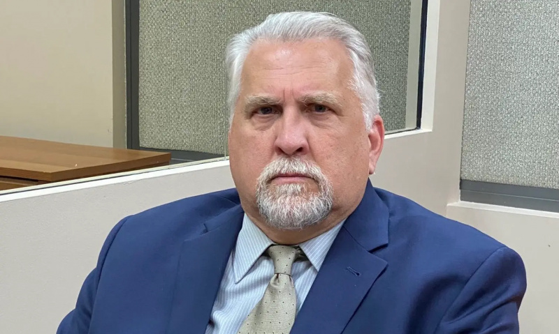Daniel Roebuck sjedi u plavom odijelu prekriženih ruku.
