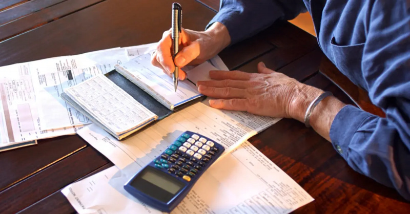 一个成熟女人的特写's hands as she sits at a table writes checks