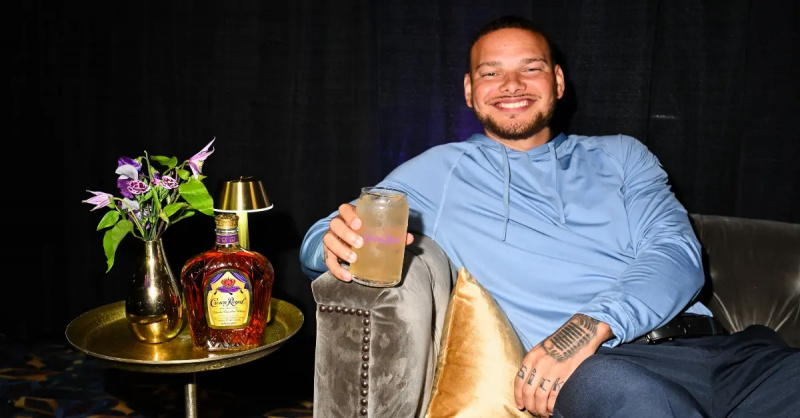 Кейн Браун улыбается, держа в руках коктейль Crown Royal.