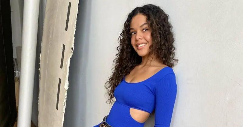 Melissa Kadas fra'A2K' wears a blue body suit and leans against a wall and smiles.