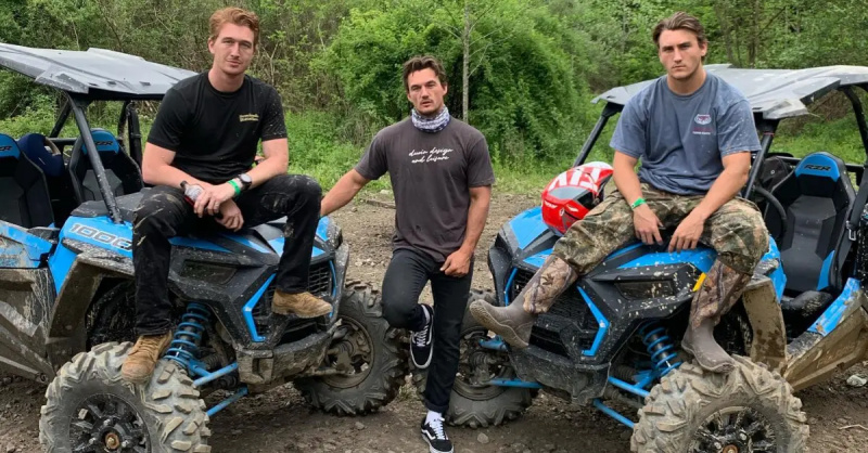 Tyler Cameron (tengah) berdiri sementara saudara laki-lakinya, Austin (kiri), dan Ryan (kanan), duduk di atas kap sepeda quad ATV.