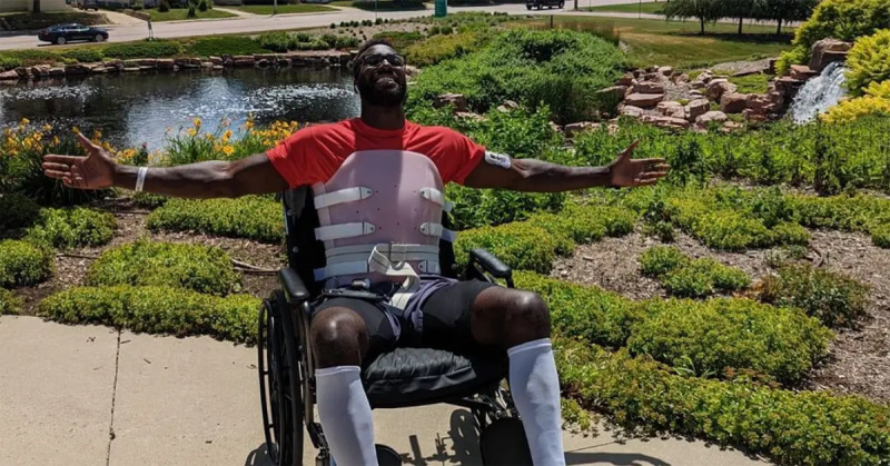 Patric Young, les bras tendus, dans un fauteuil roulant dans un jardin.