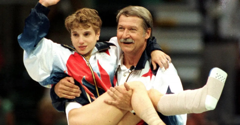 Bela Karolyi nešioja Kerri Strug