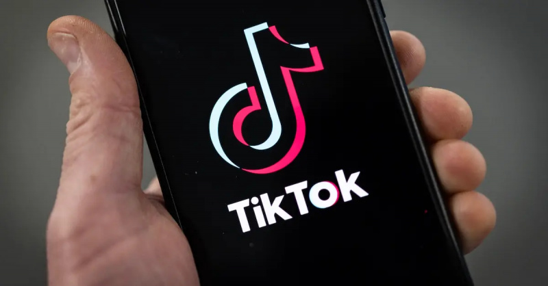 En person som håller en smartphone med en TikTok-logotyp visas.