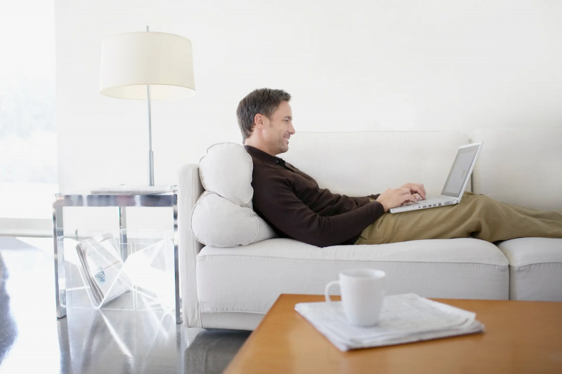 Isang lalaking nagpapahinga sa sofa at nakatingin sa laptop