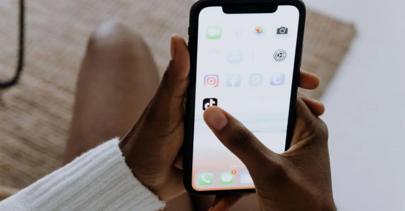 Osoba klikající na aplikaci TikTok na svém telefonu.