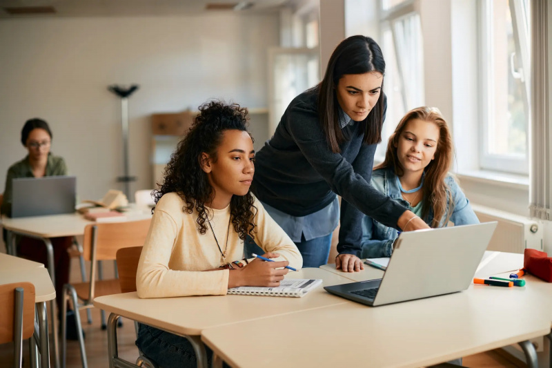 Uma professora do ensino médio auxiliando seus alunos no e-learning no laptop na sala de aula